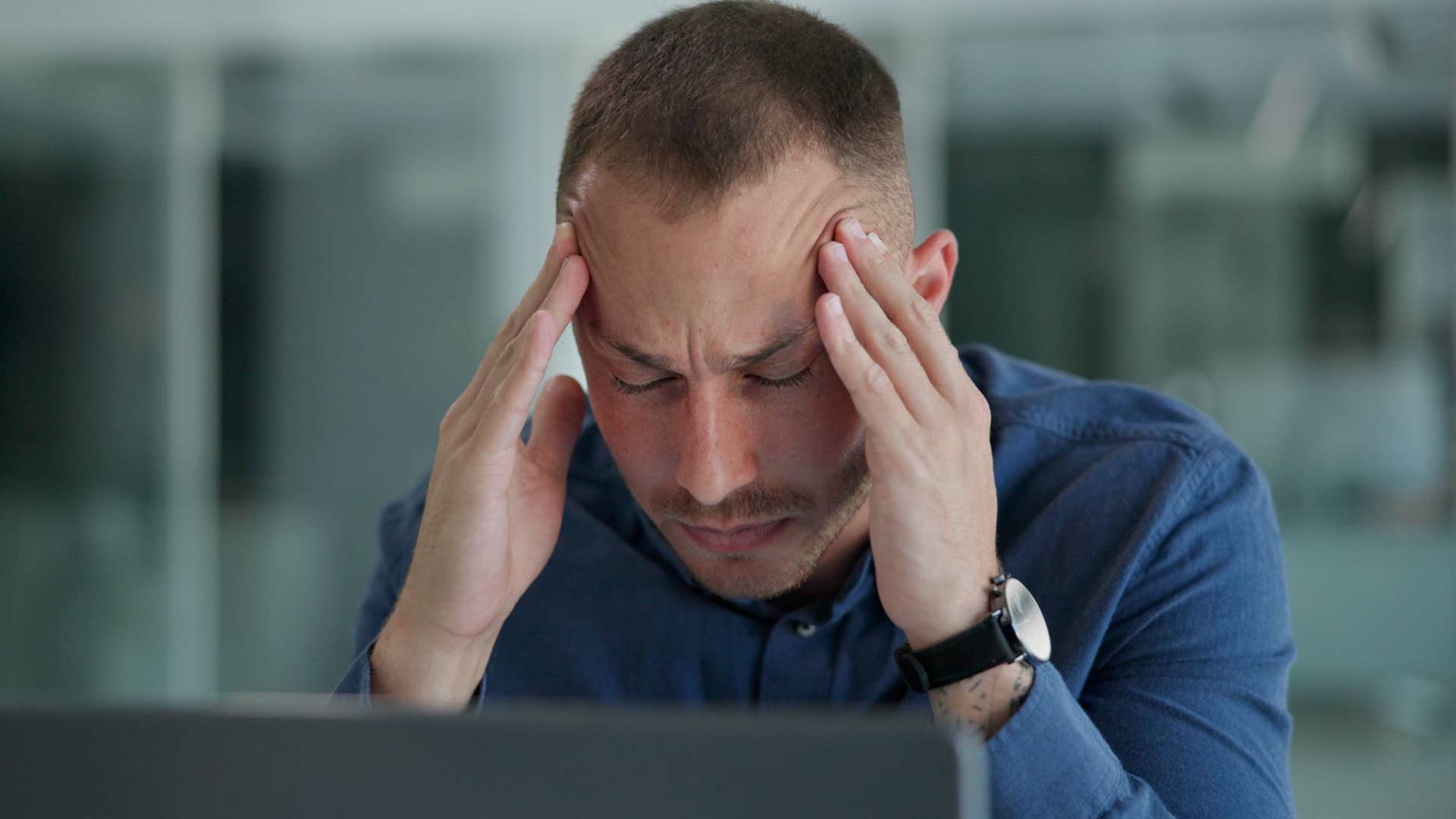 Perfectionist man holding his head sitting at a work desk