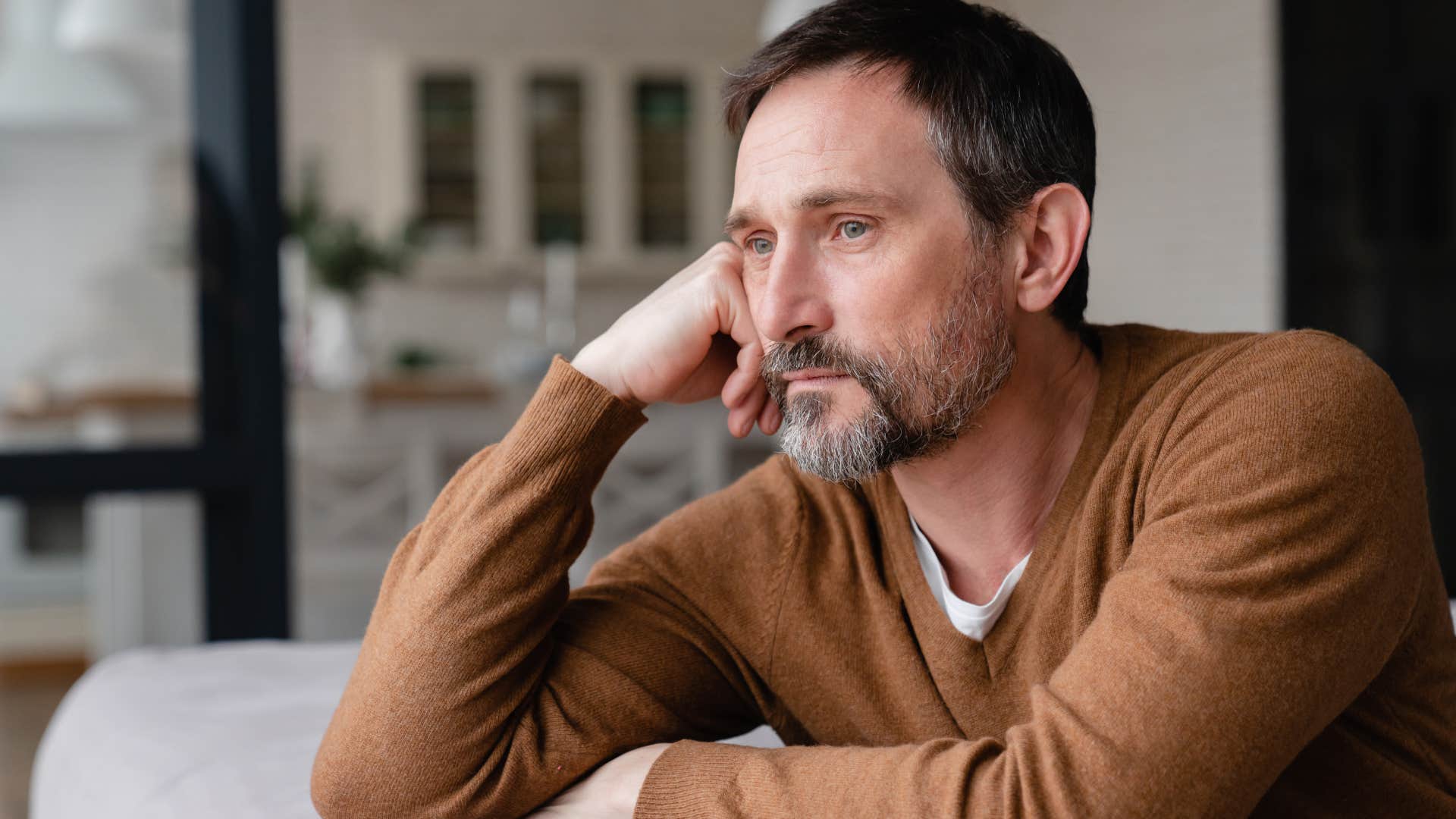 Man who's burnt out from societal expectations looking out a window.