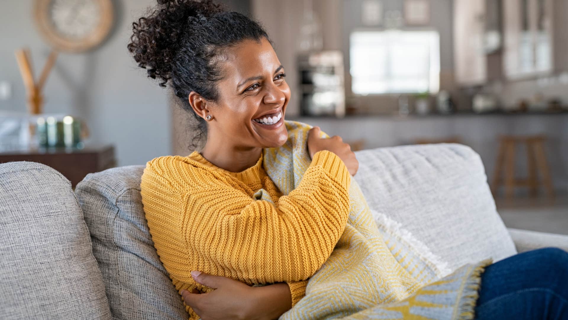 Woman who doesn't feed into consumerism smiling on her couch.