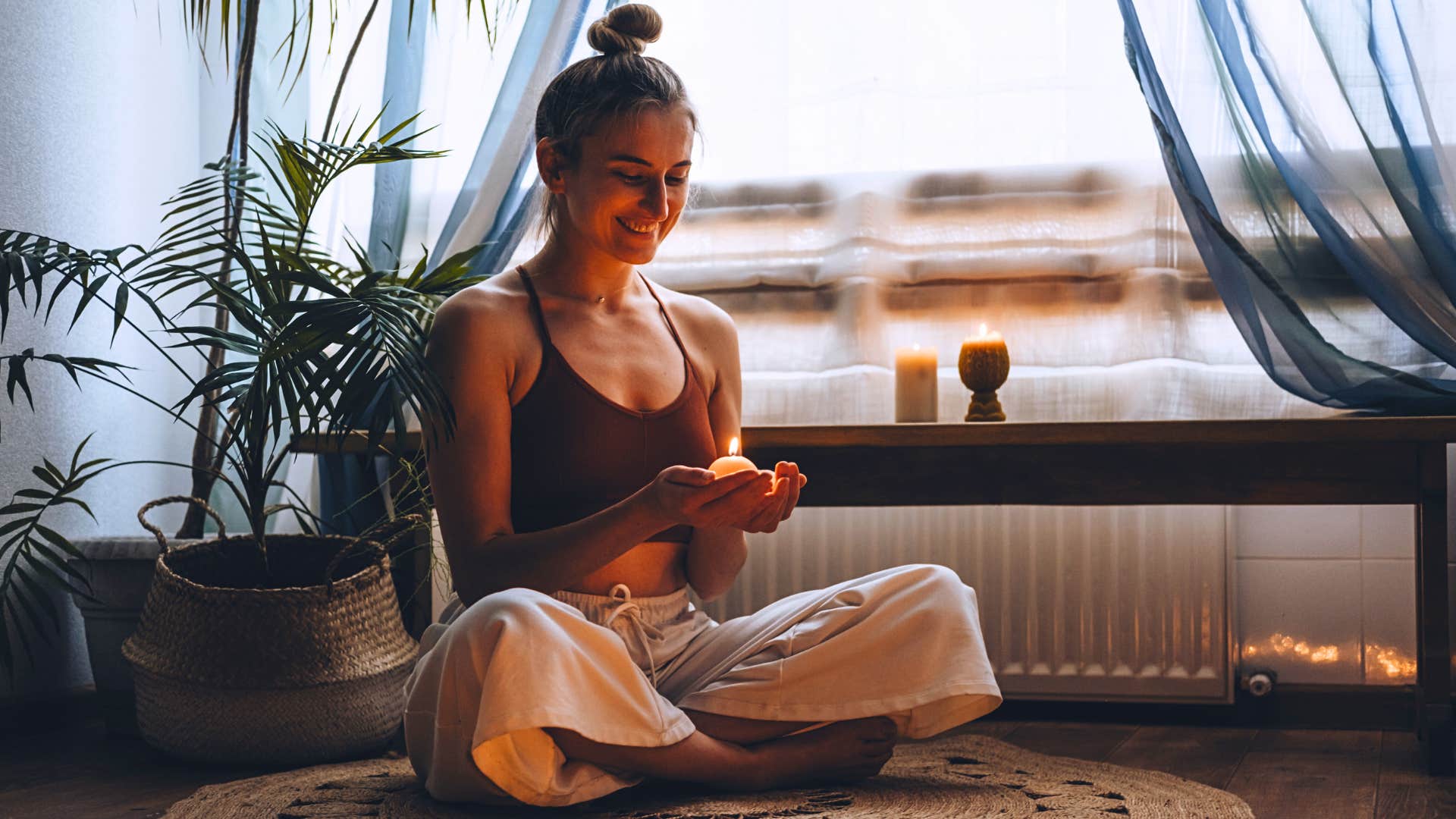 woman sits on floor with candle and incense around her home