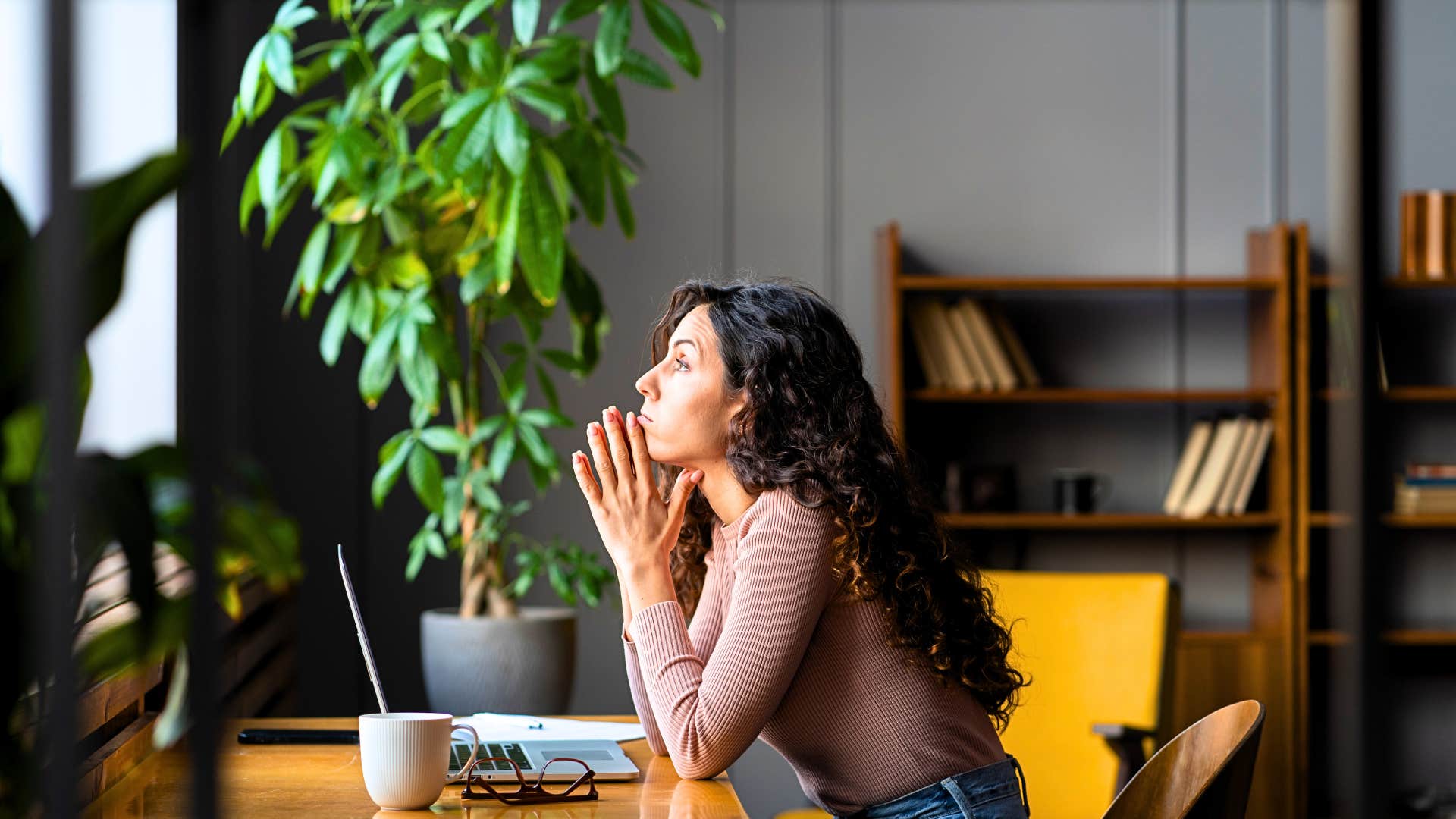 woman with healthy thriving plants looks out the window in her home