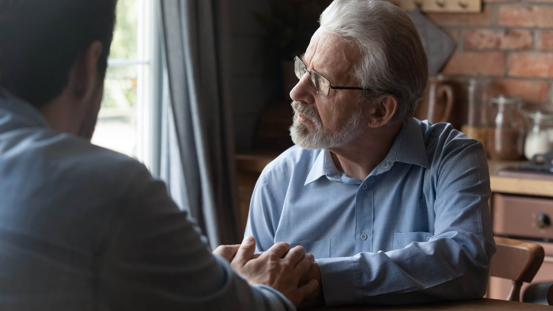 Man saying "when I was your age" to his adult son while holding his hand.