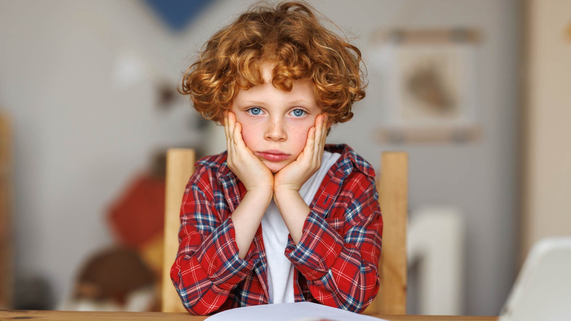upset little redhead boy with his hands on his chin