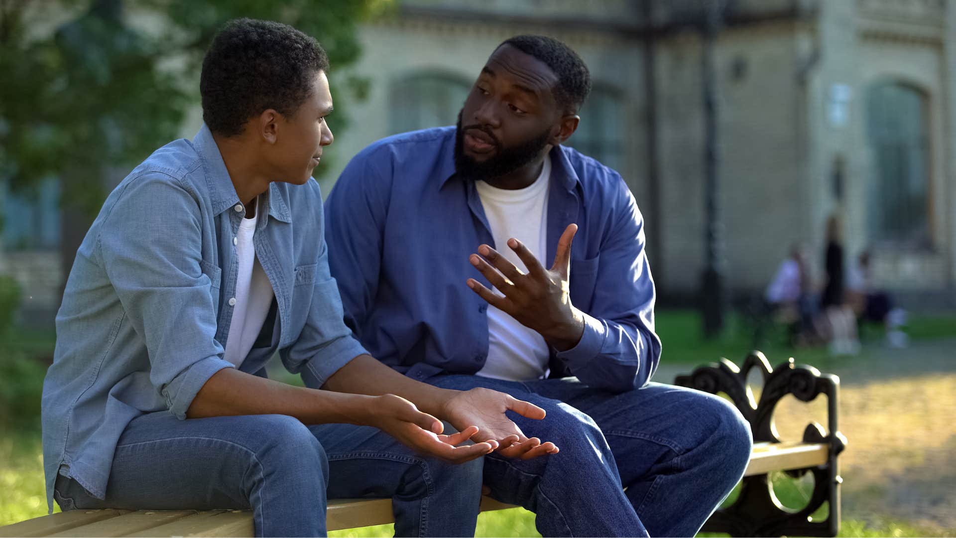 father and son sitting on the bench as father in dark blue jacket tells son in light blue jacket that he doesn't have it hard