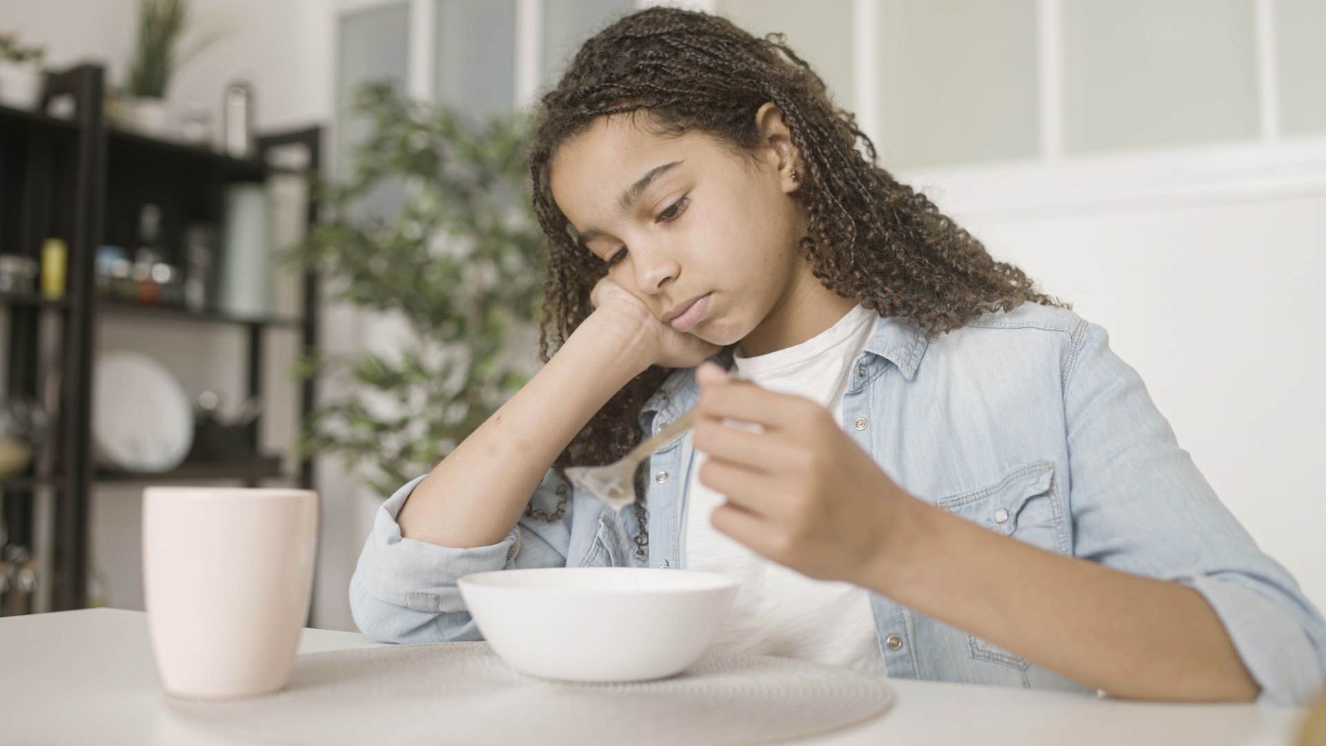 girl with jean jacket and white shirt eating miserably as parents told her she's not leaving this table until she finishes her food