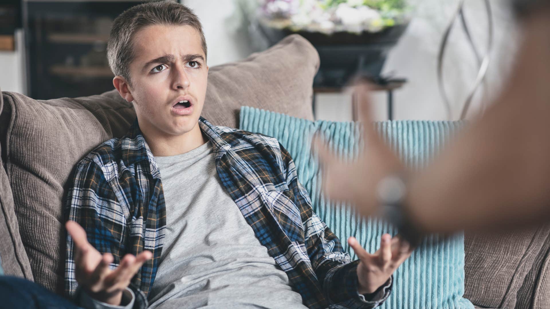 son in gray shirt in disbelief as father shouts at him to stop acting out because he's embarrassing him