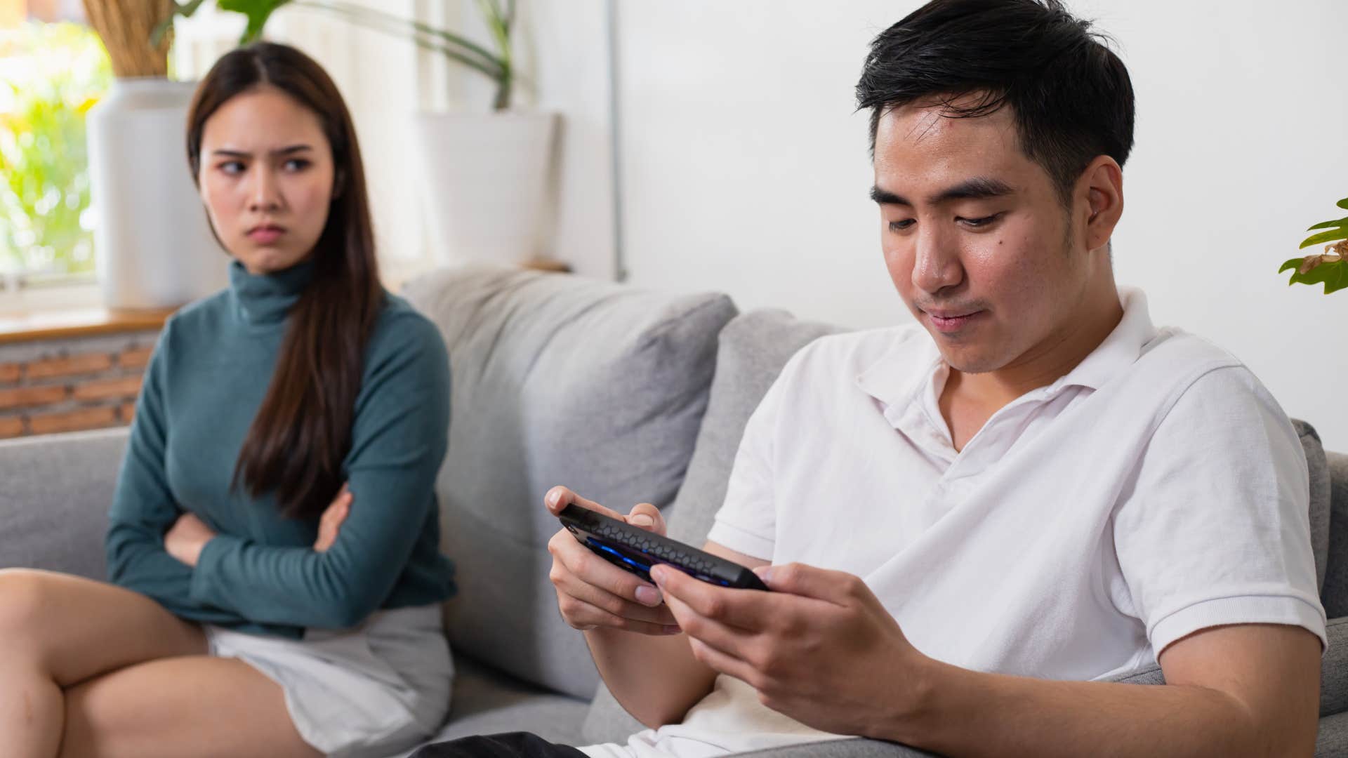 lazy husband playing video game next to very angry wife
