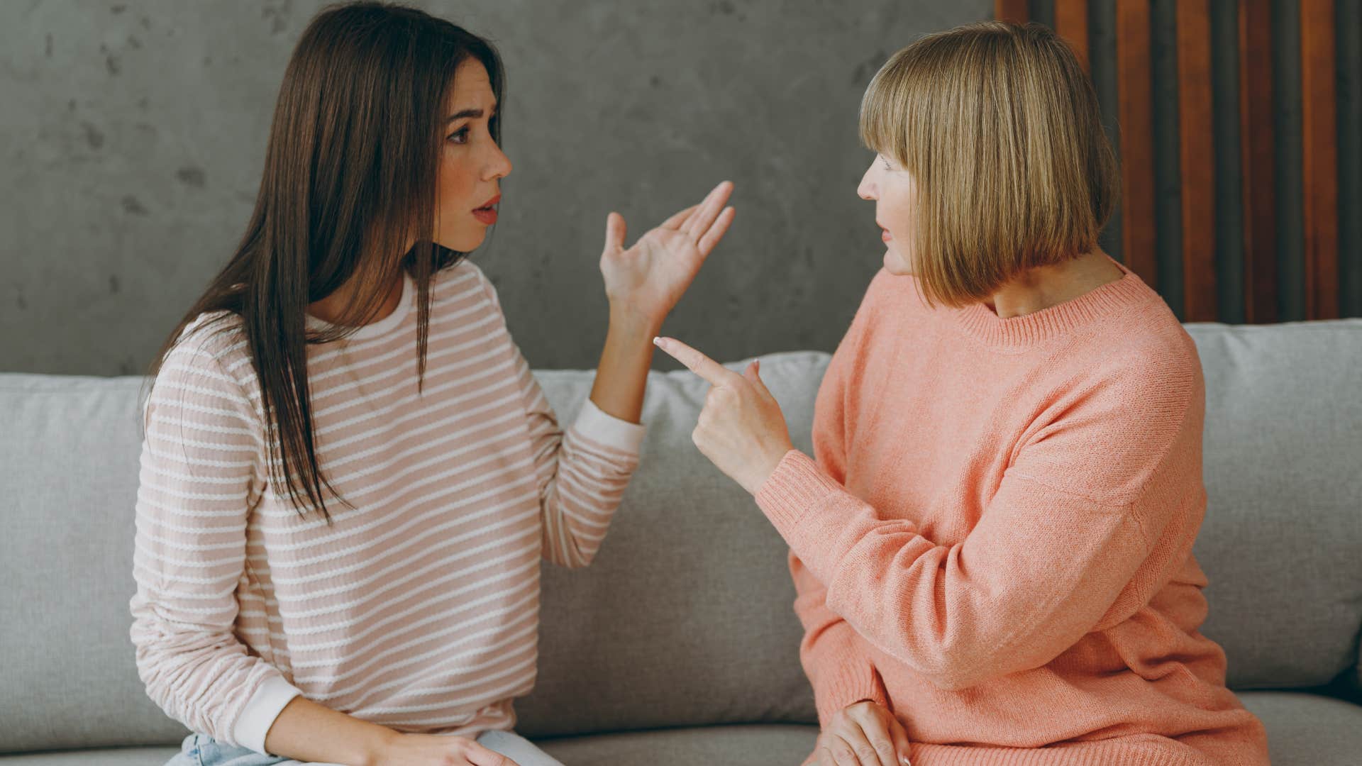 Woman saying "I'll pay you back" to her upset mother on a couch.
