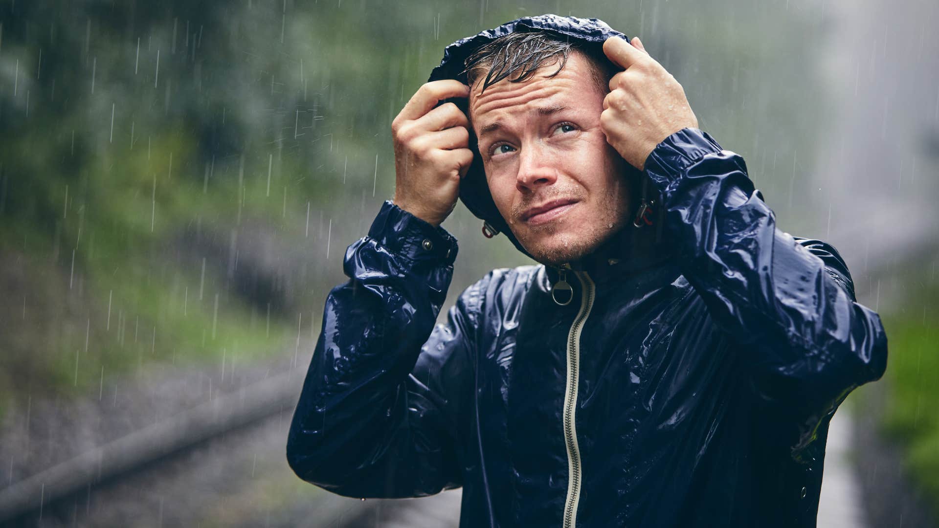 man thinking it's a real gully washer pulling hood over raincoat