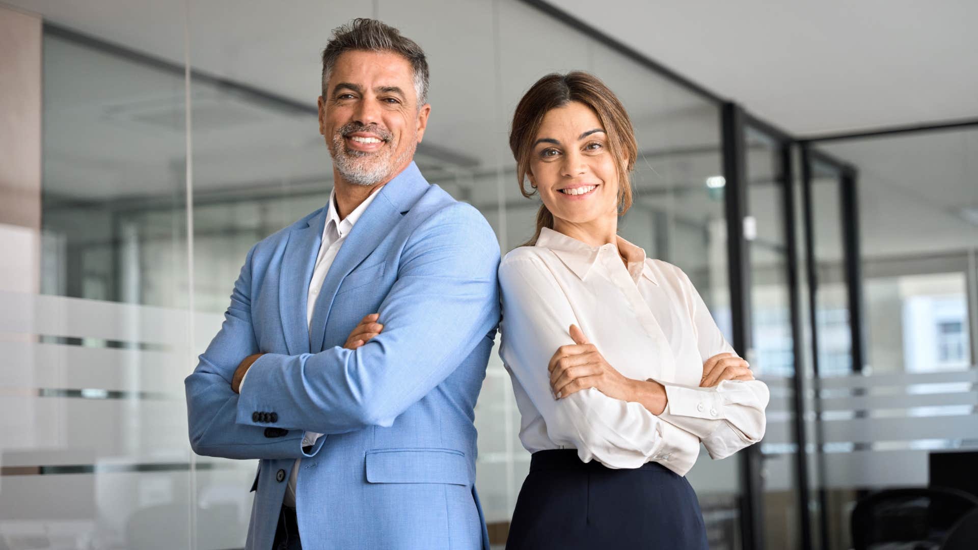 hardworking couple in the office standing back to back smiling