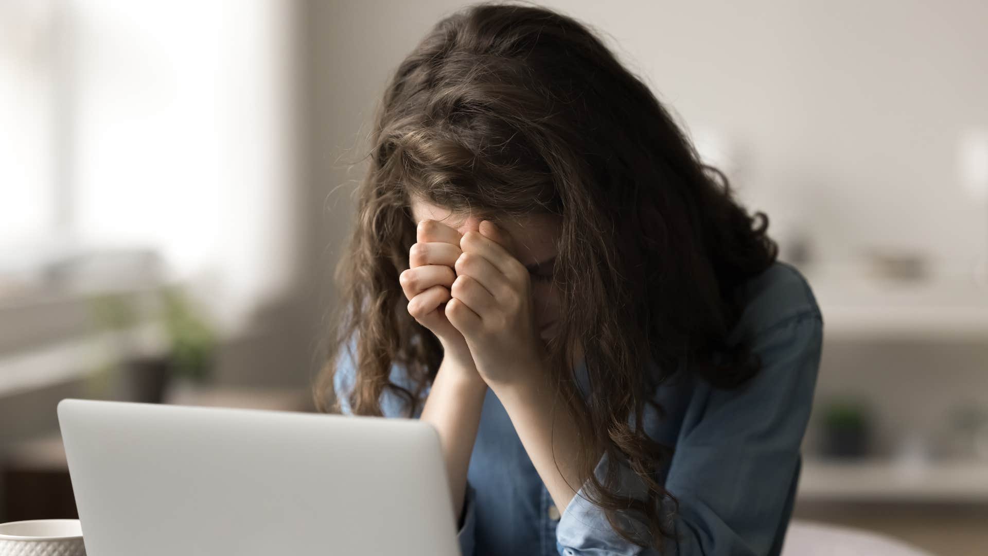woman putting head in hand as she always feels anxious as she's working on laptop