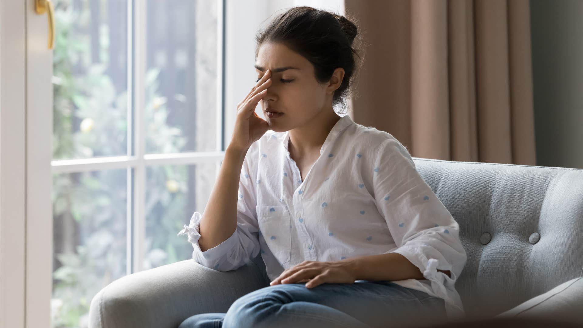 woman in white shirt feels drained as she rubs face with hand as she sits down