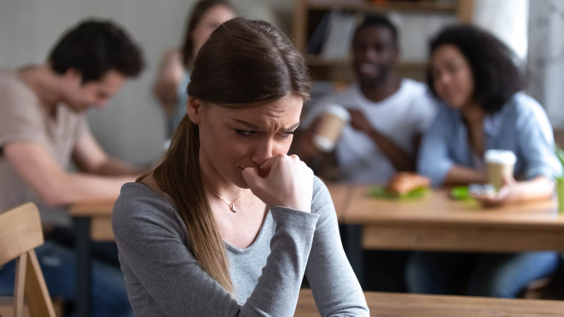 woman in gray shirt sitting further away from friends and looking upset as she feels like she can't be vulnerable with her loved one's