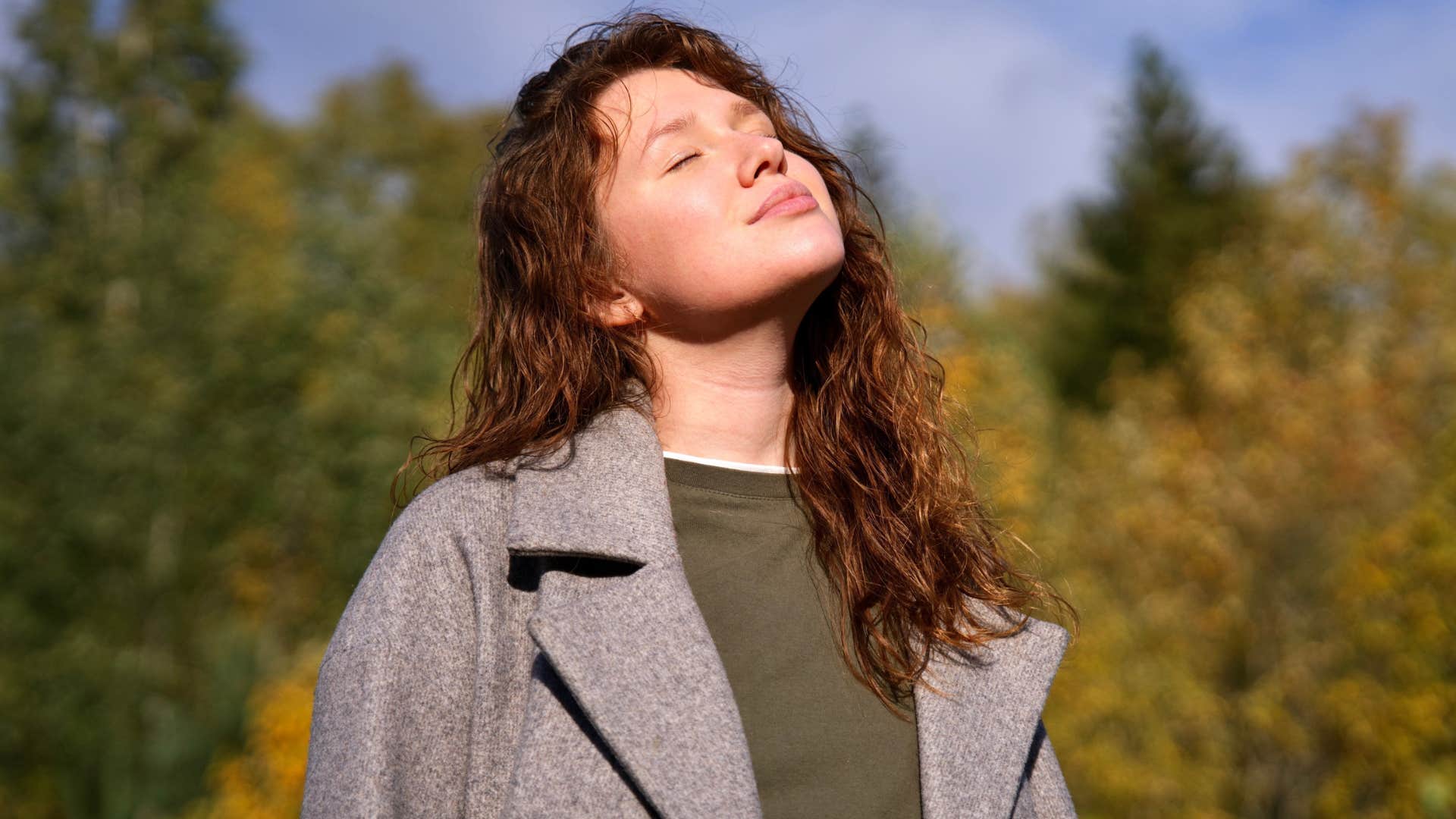 Woman with strong gut instincts smiling and closing her eyes outside.