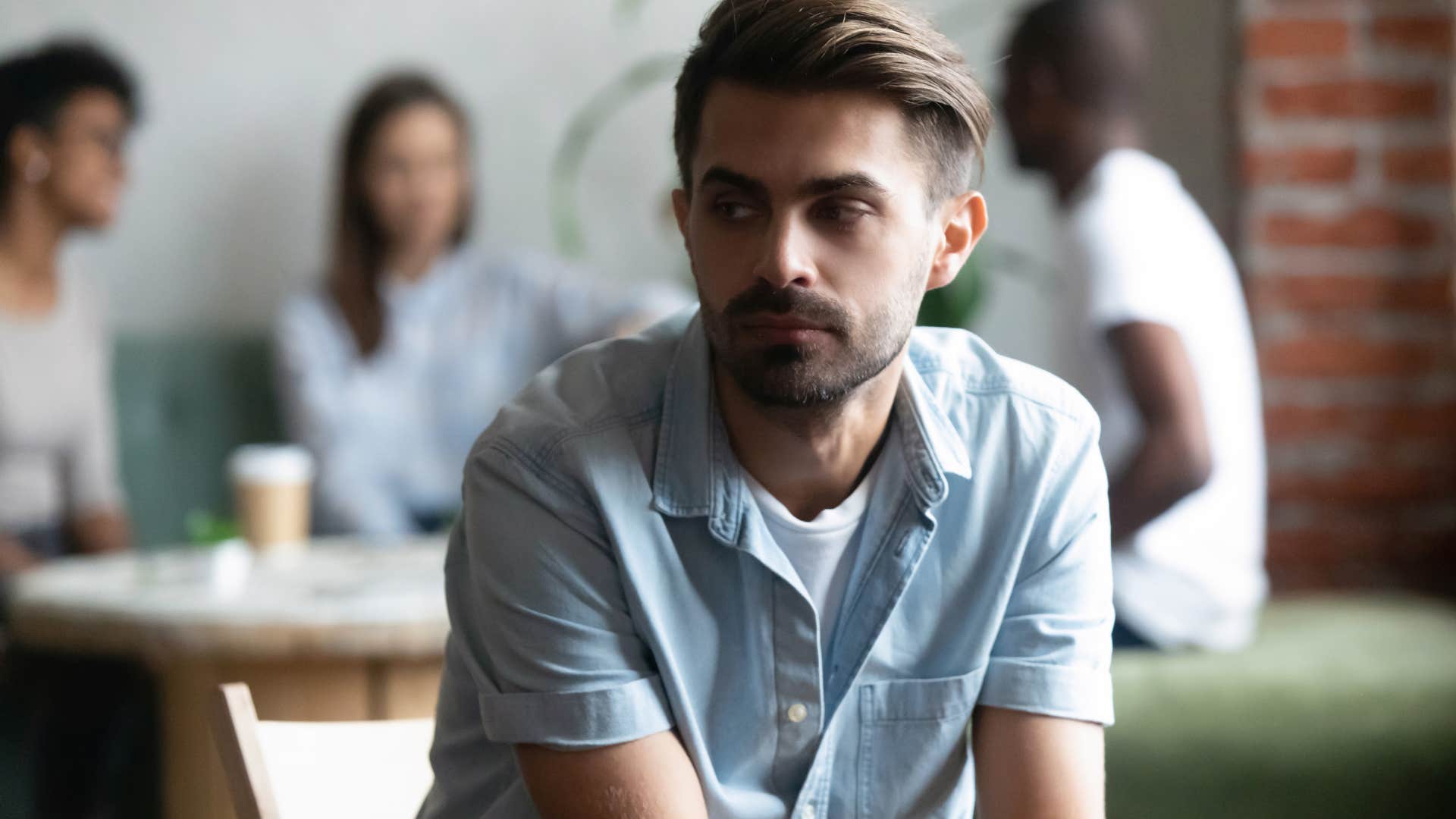 sad man sitting behind friends feeling lonely around them