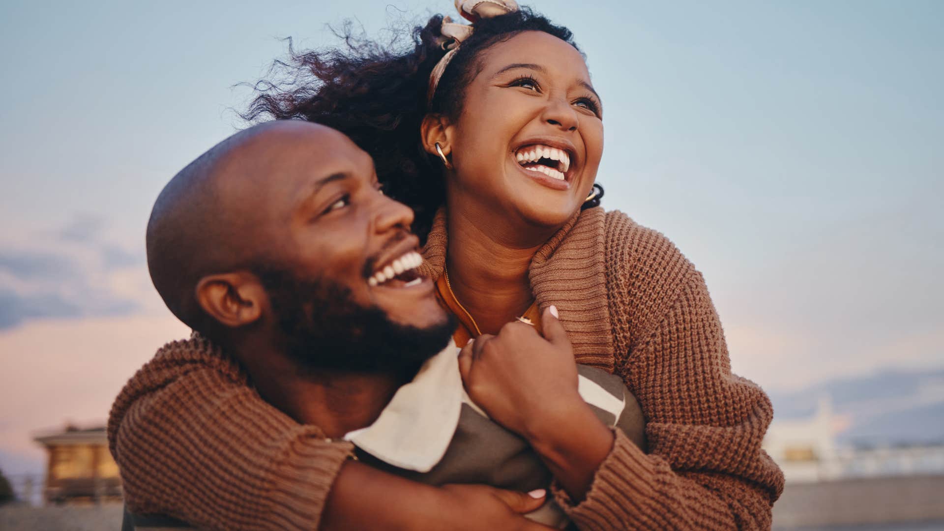 Woman who gives compliments often smiling and hugging her partner on a beach.