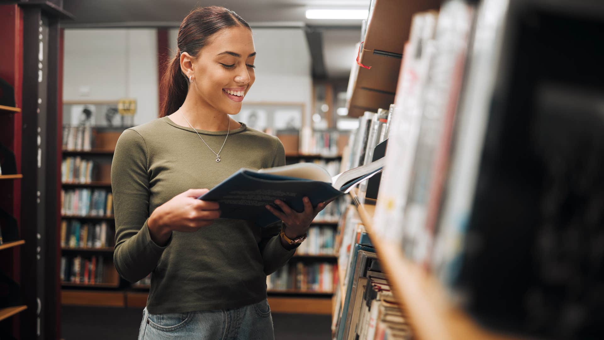smiling happy woman in library reading a book