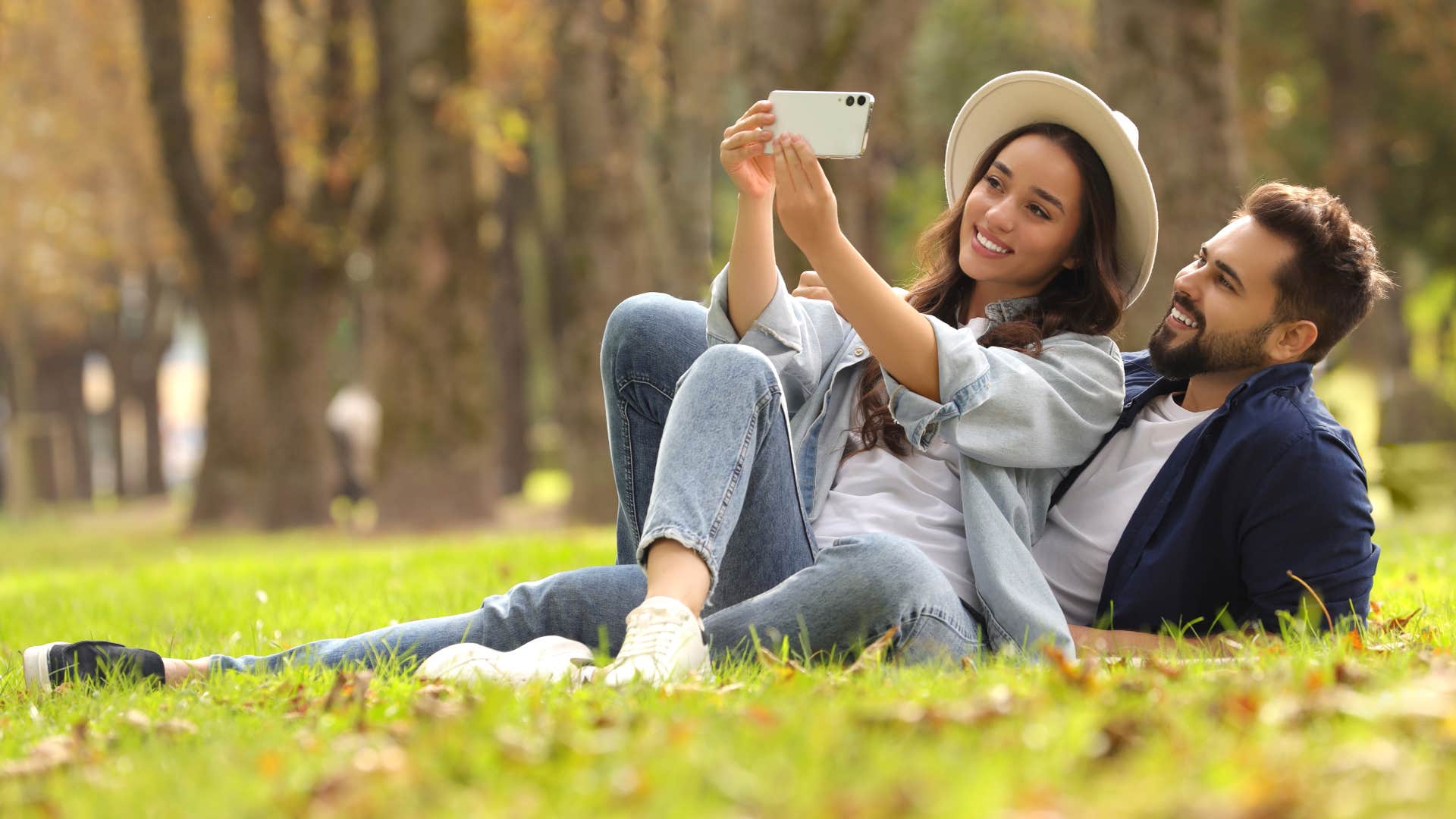 couple laying on grass as they copy pose that they saw on social media and take a selfie together