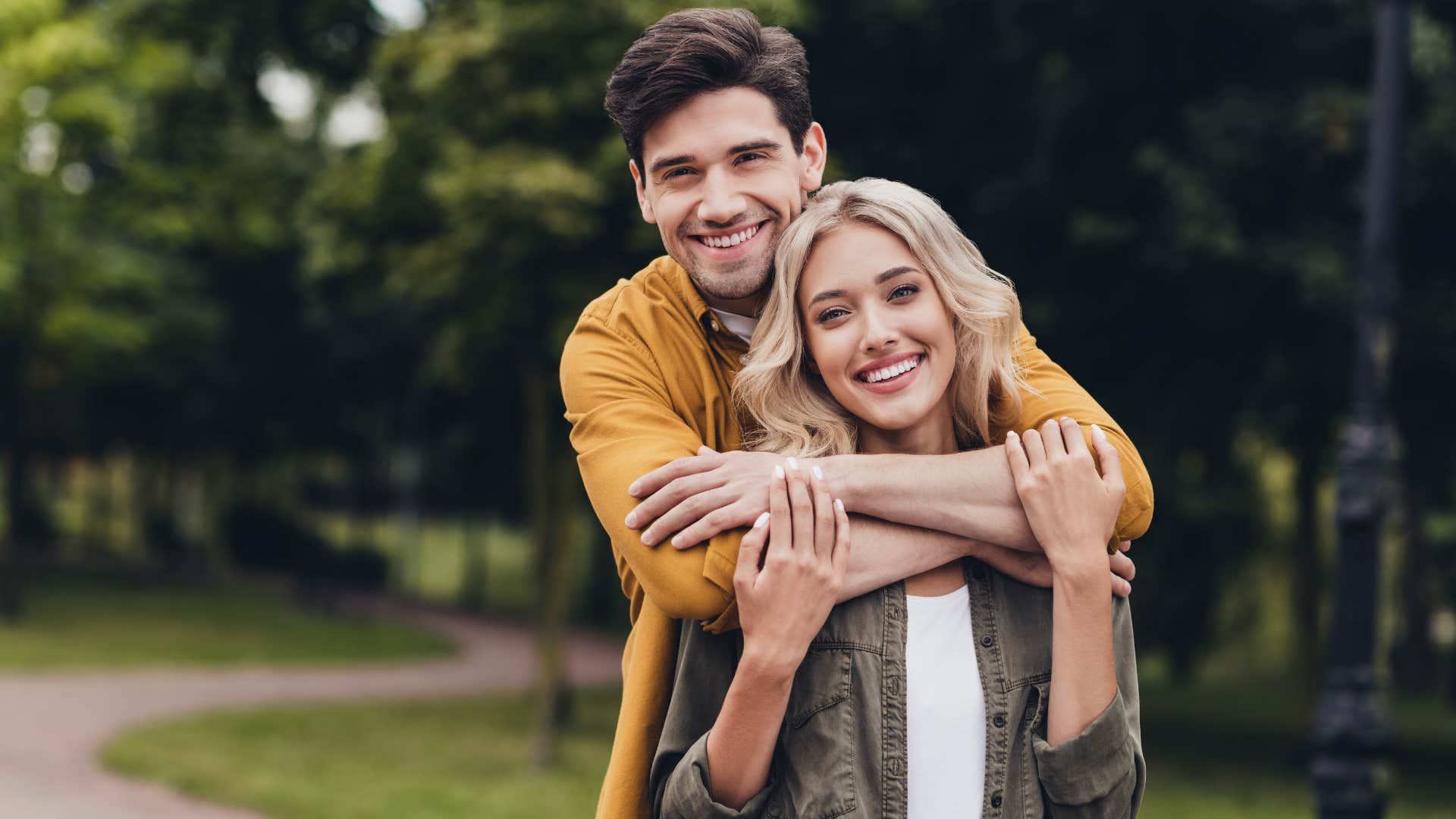 man hugging woman with blonde hair from behind as she looks like ex partner
