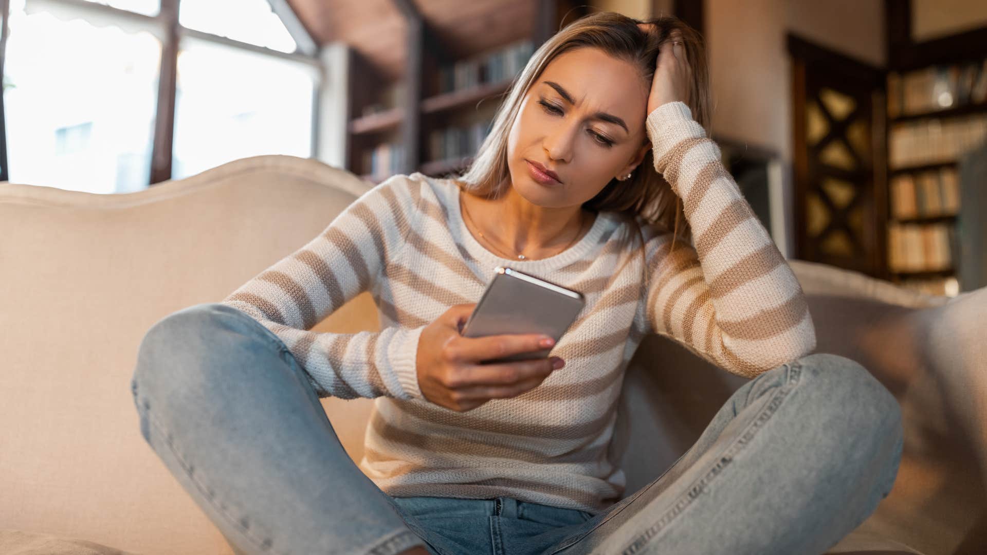 woman in stripped shirt looking upset on the couch as ex randomly texts her hi