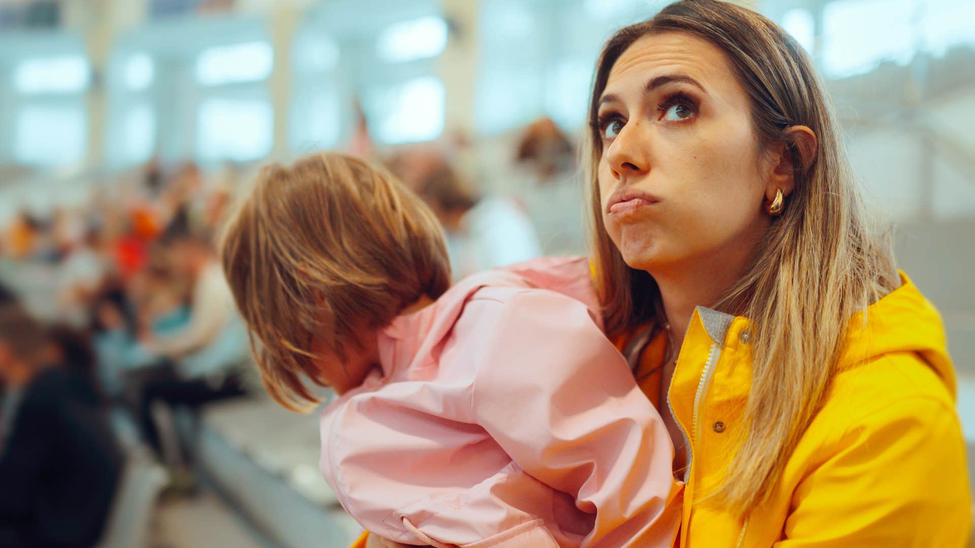 Woman overwhelmed in loud parties and packed crowds sitting with her baby in an airport.