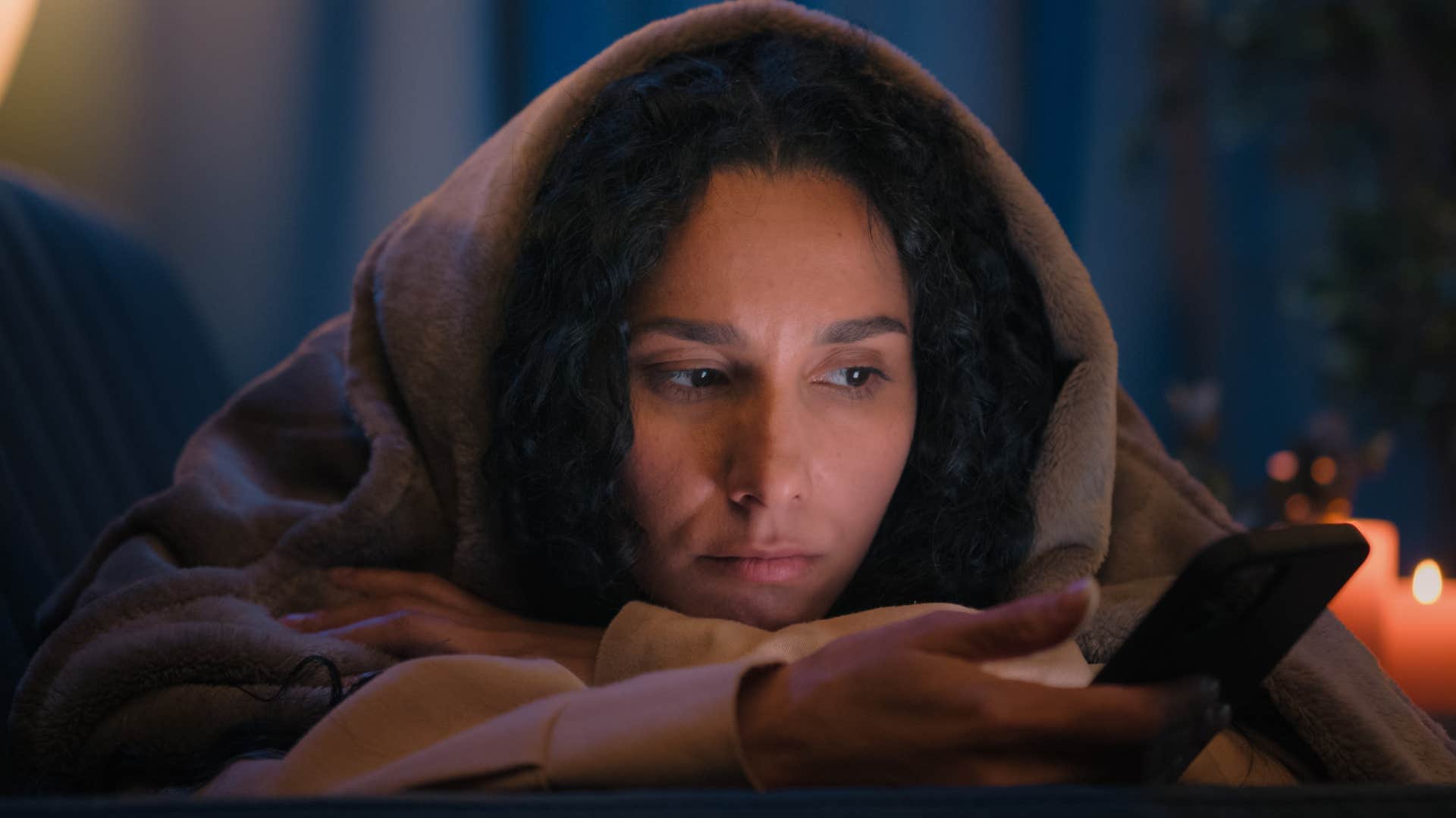 Woman chasing trends to fit in scrolling on her phone in a dark room.