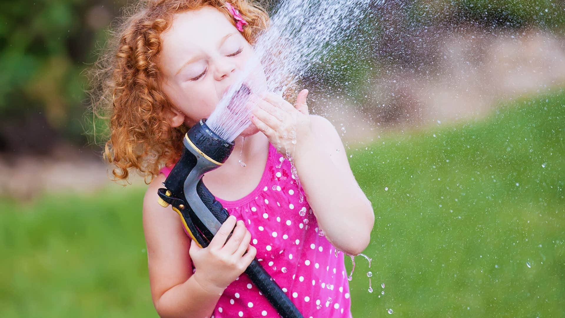 girl drinking water from a garden hose