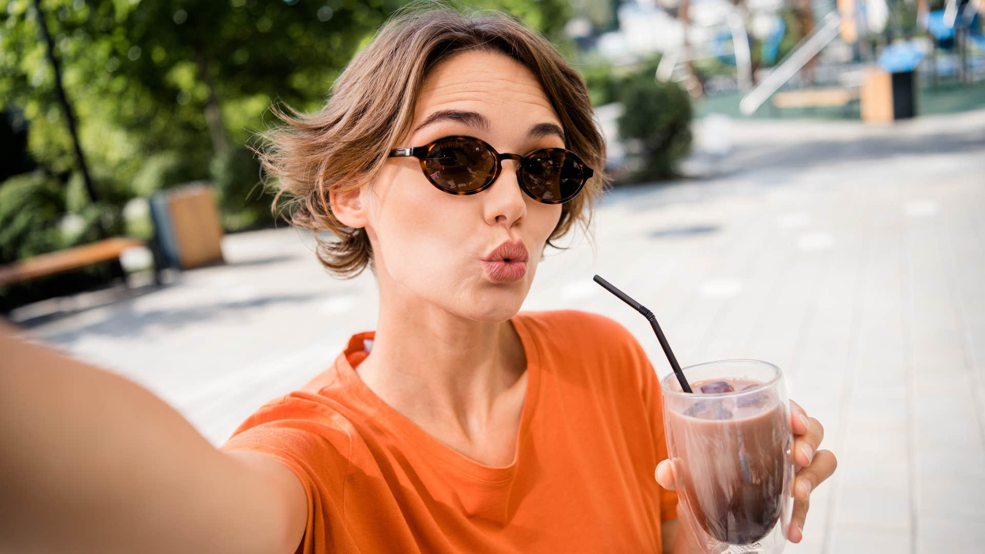 woman in sunglasses sipping drink as she posts her daily routine 