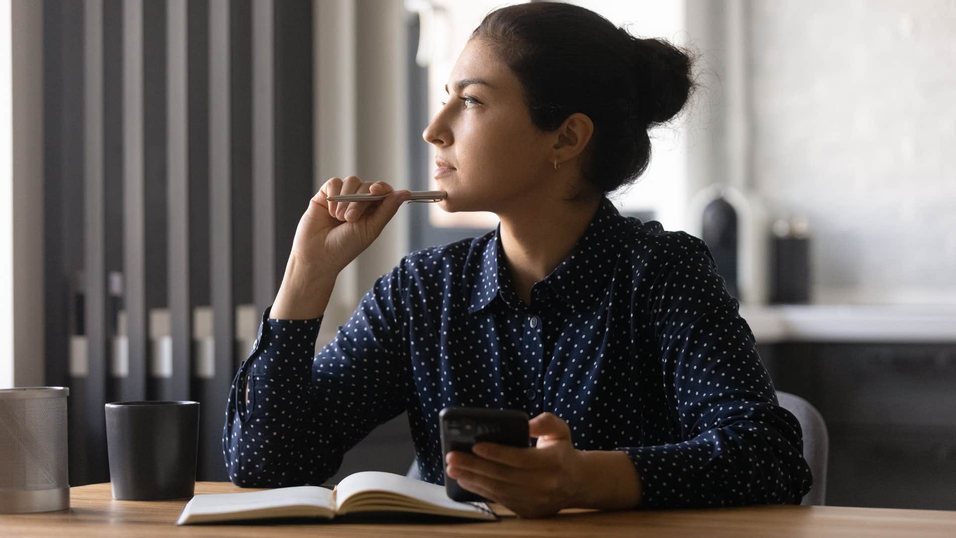 woman coming up with new years resolution post as she thinks with phone in hand