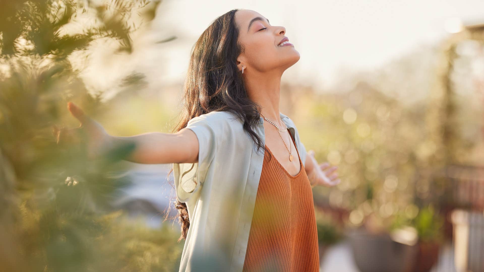 woman at peace as she meditates outside with outstretched hands