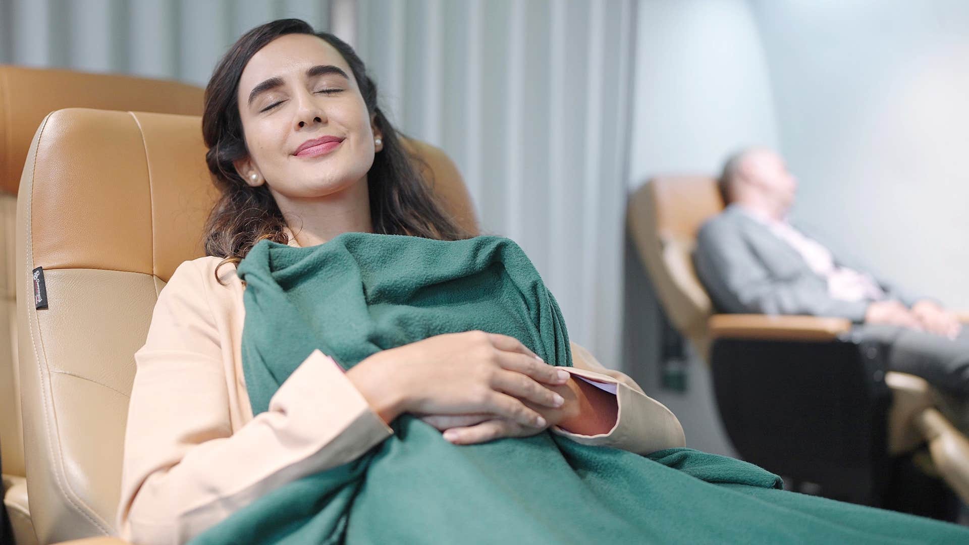 woman asleep smiling in first-class plane seat