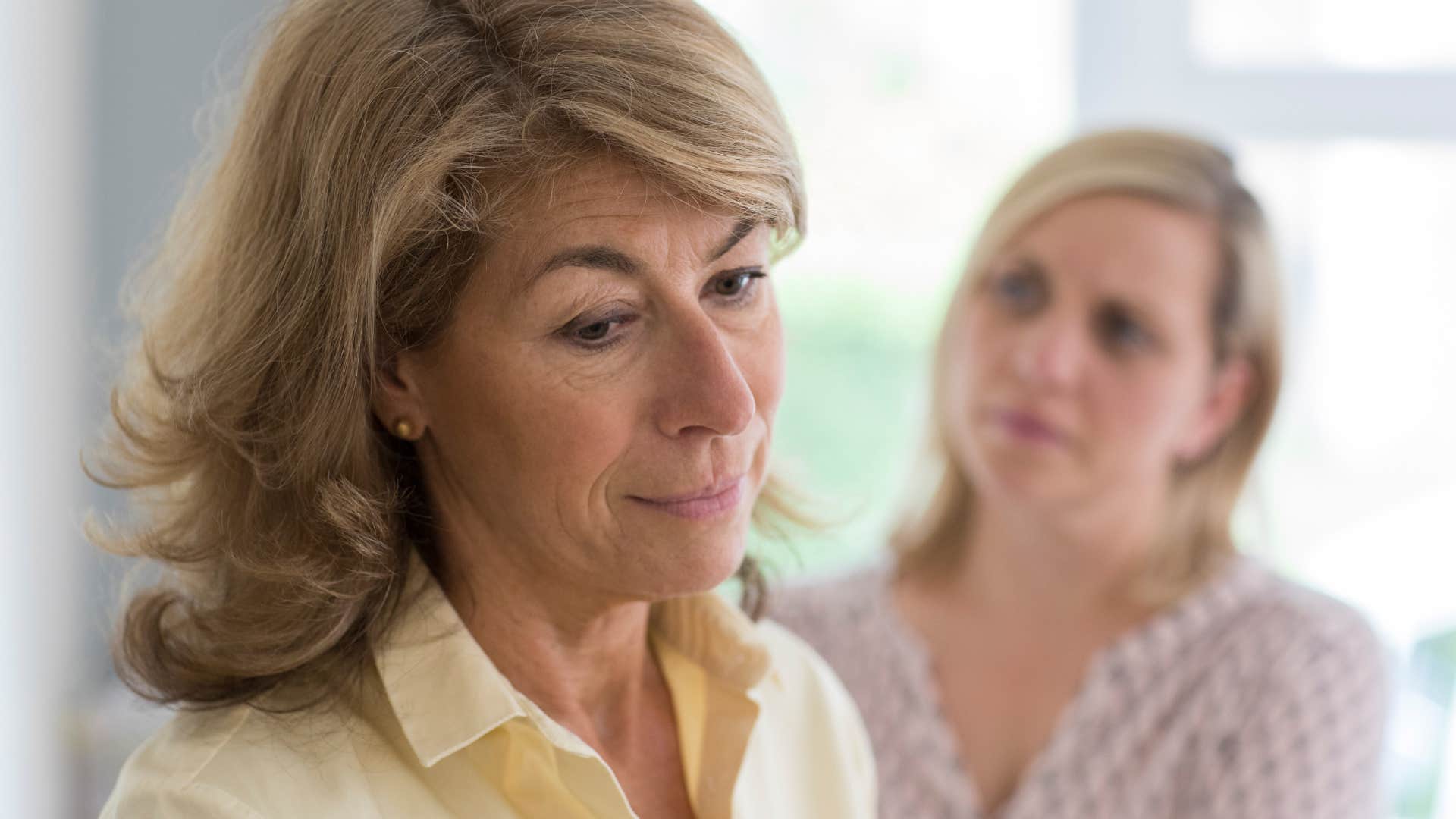 Woman looking at her mother who's talking poorly behind their back.
