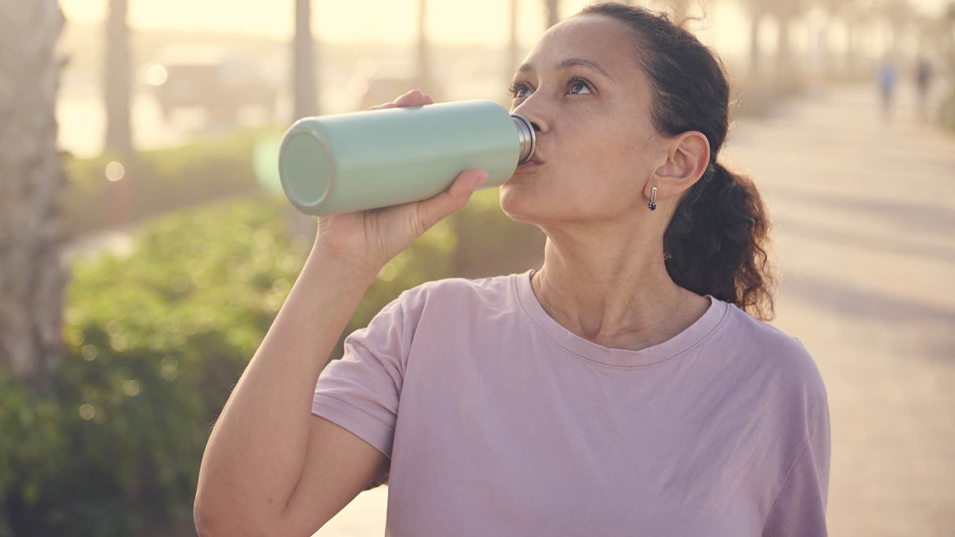 woman drinking from a reusable water bottle outside