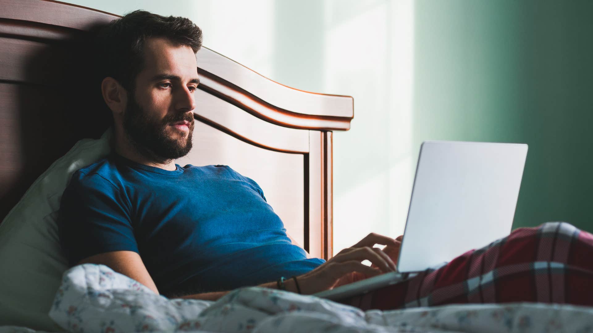 man working from bed on his laptop