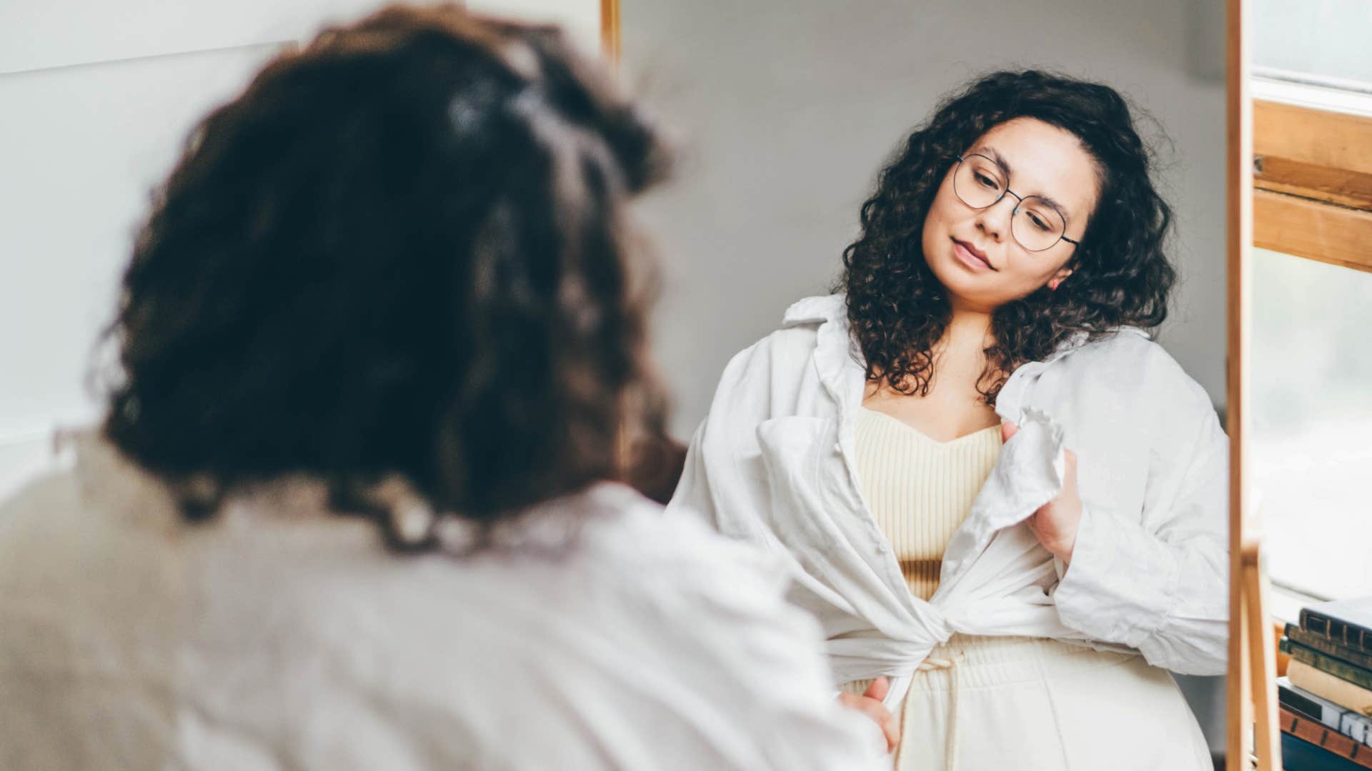 self-conscious woman looking at her body in mirror