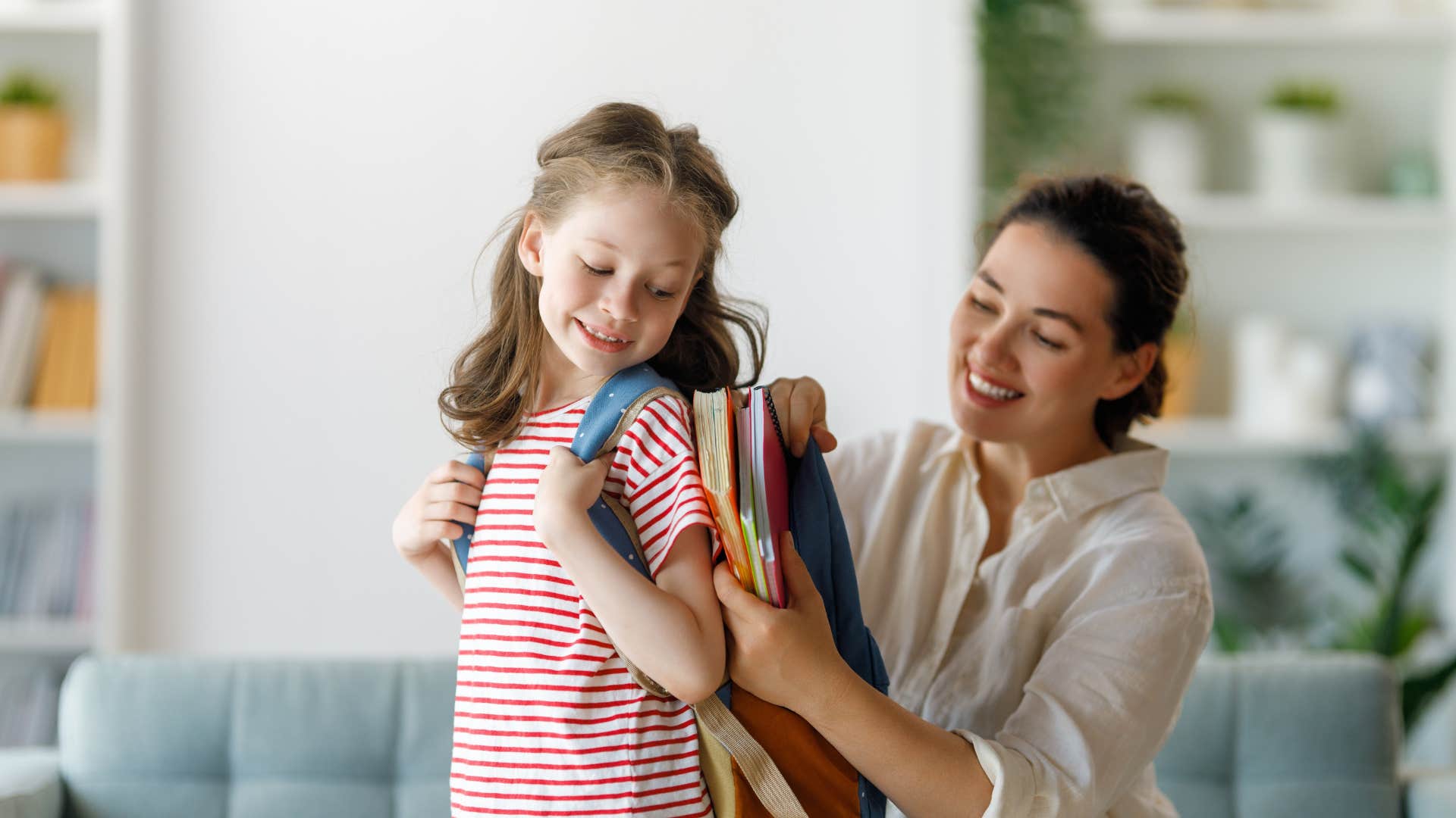mom helping young daughter with backpack for school