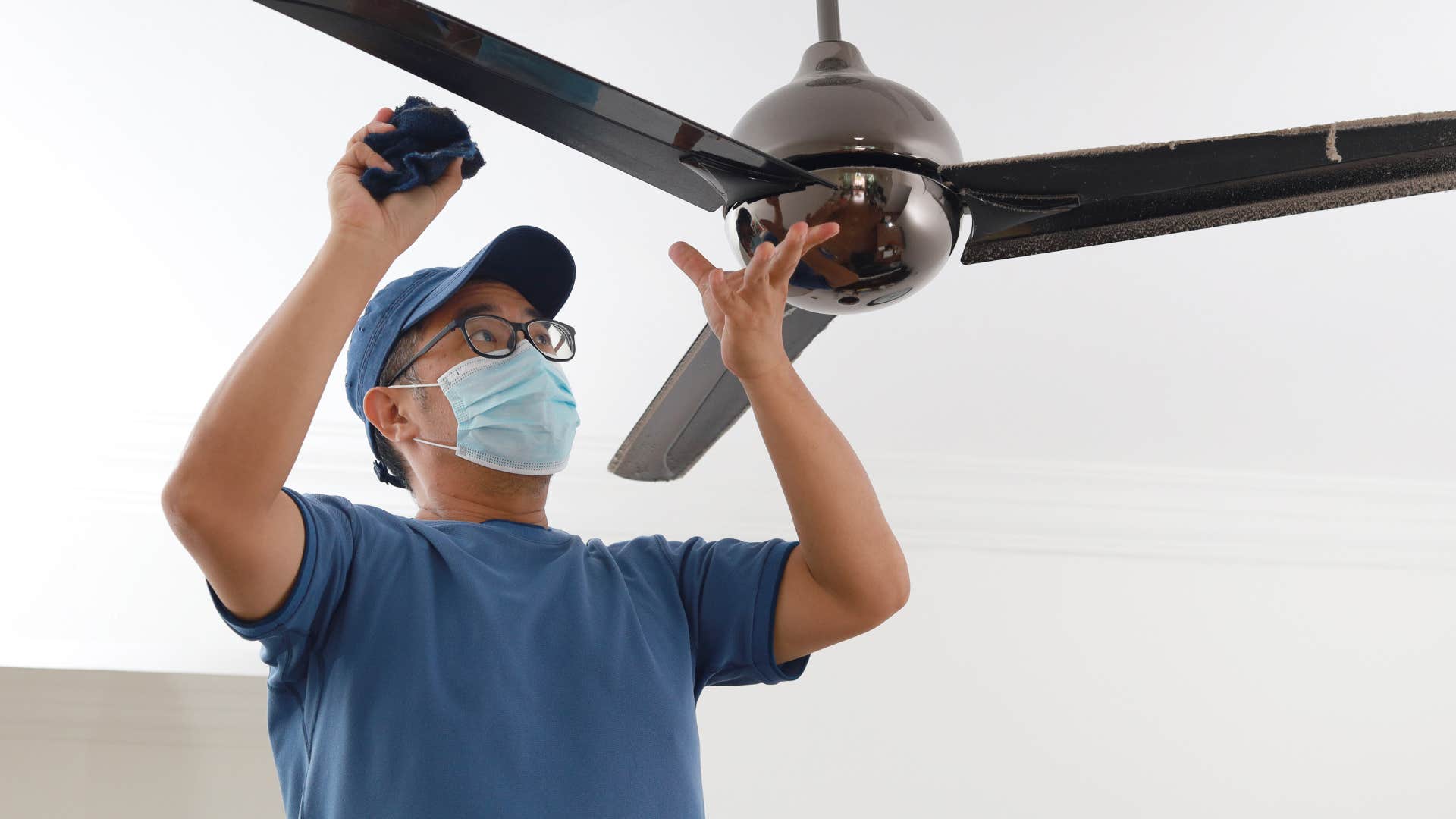 man cleaning the dust on the ceiling fan at home