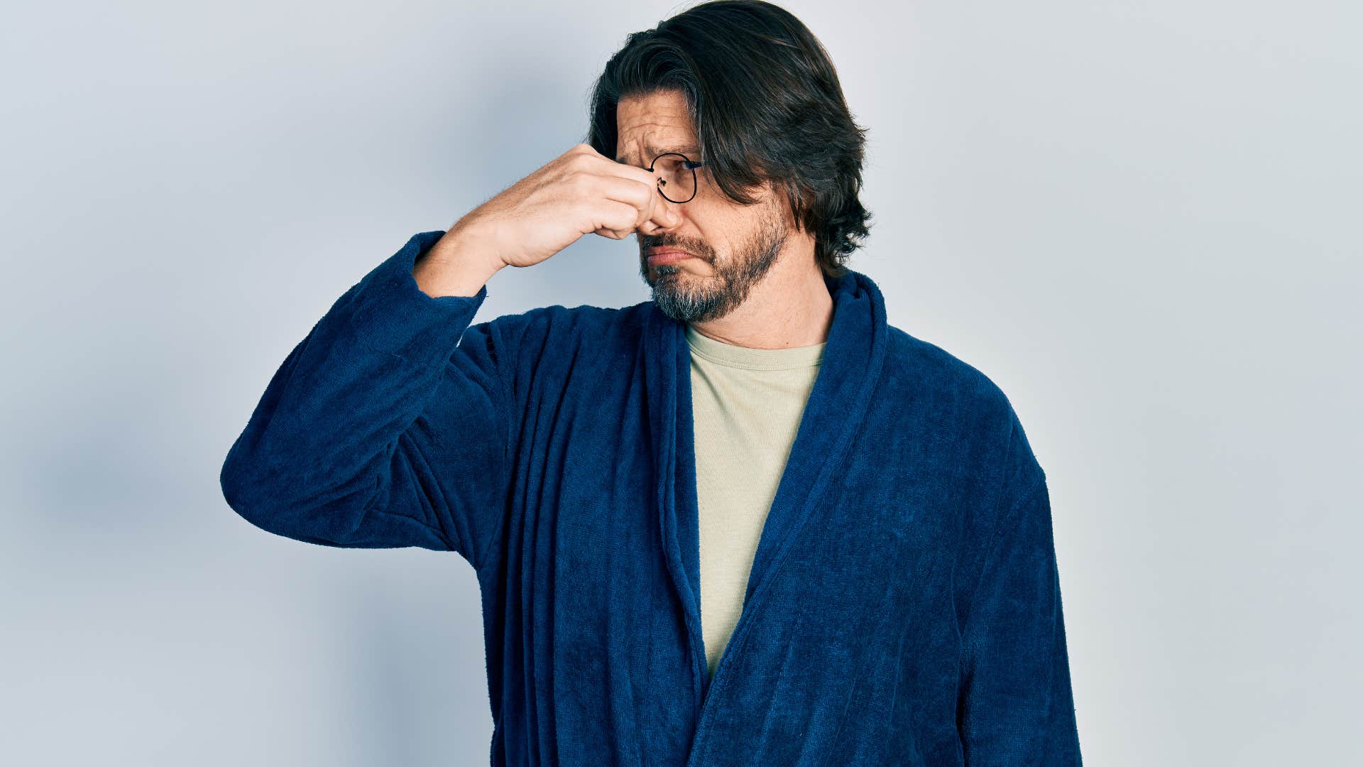 man in a bathrobe plugging his nose near an unclean toilet