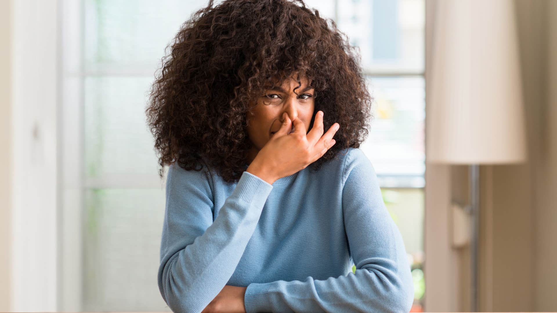 disgusted woman holding her nose smelling something gross