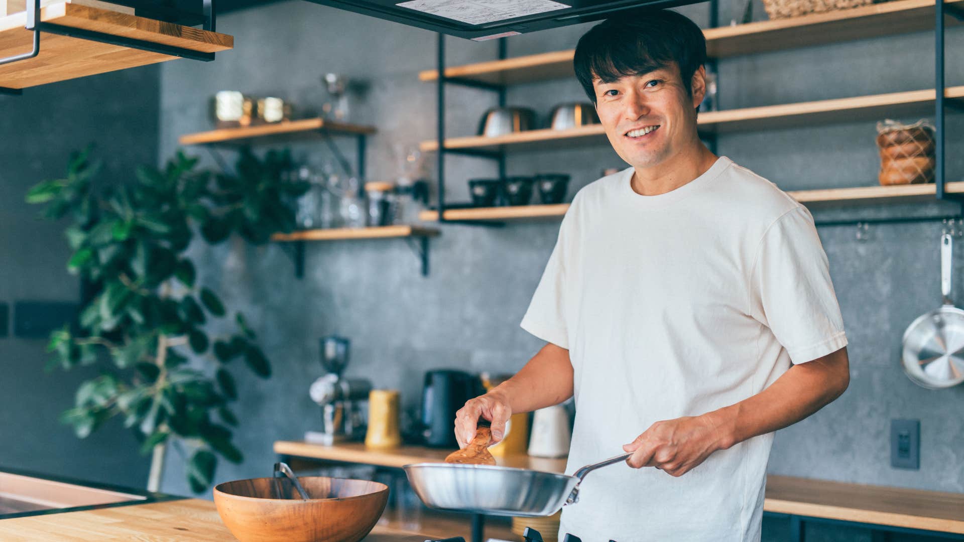man providing acts of service as he cooks in white shirt and stares at camera