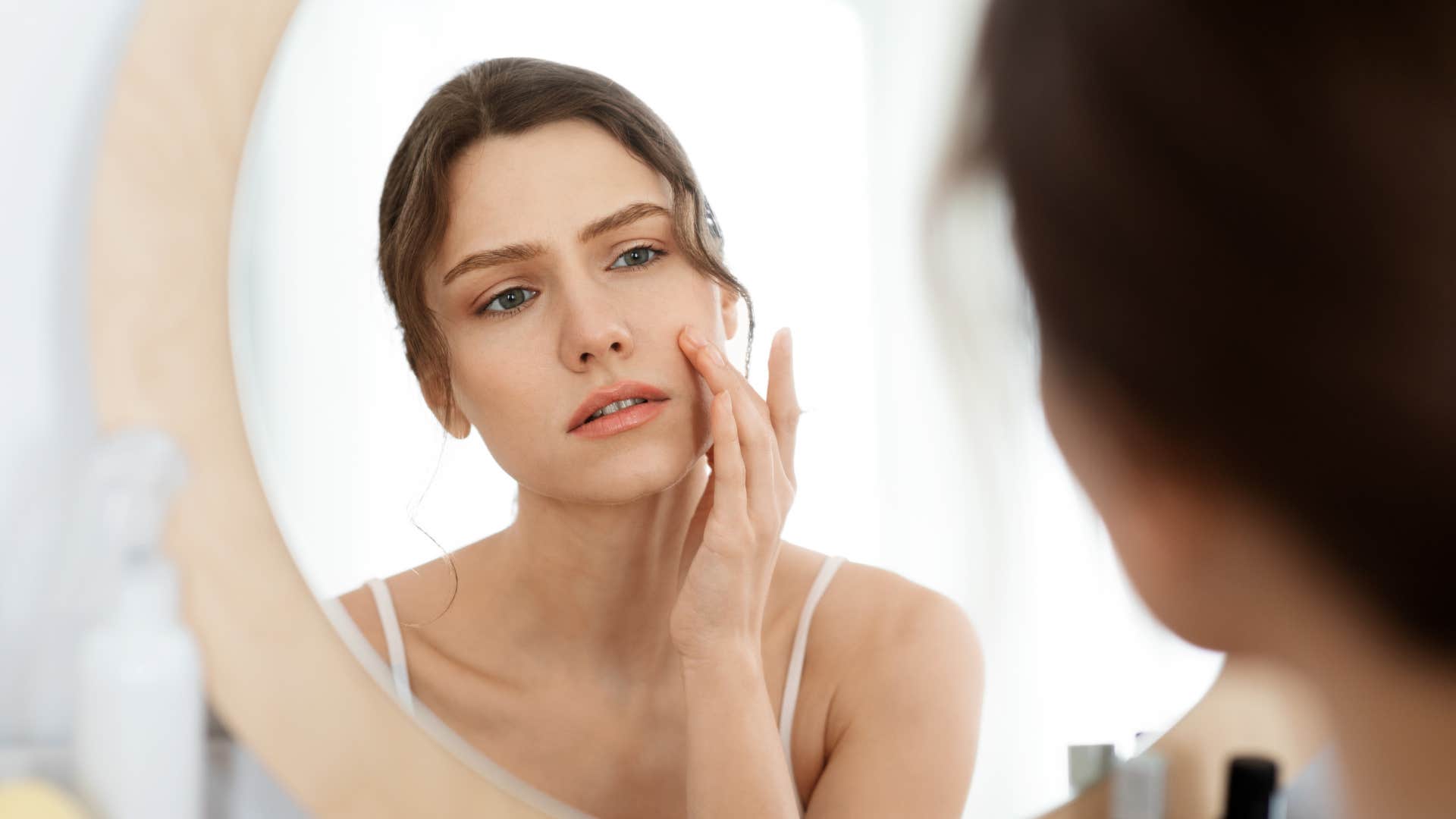 woman looking at acne on her face in the mirror