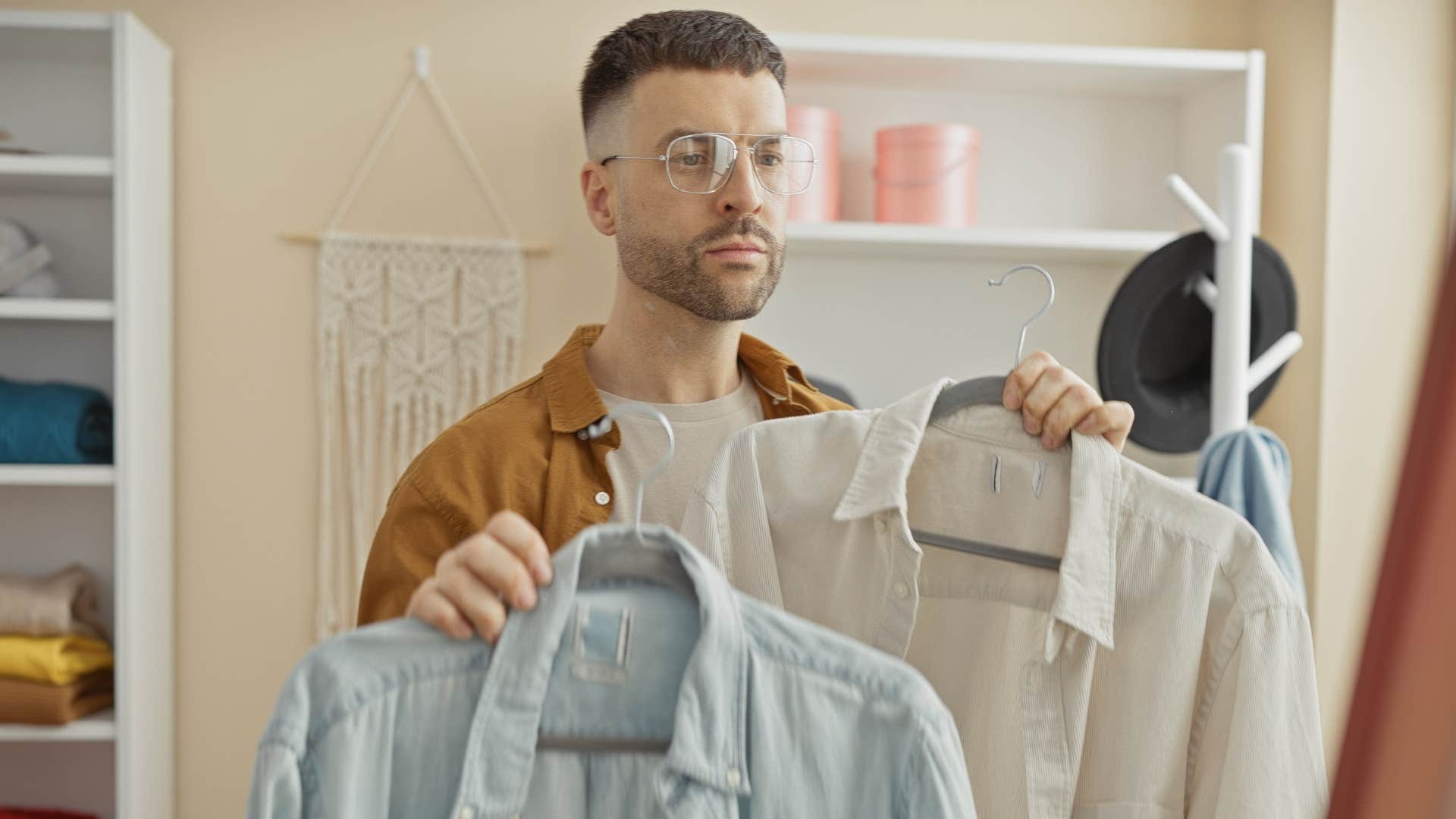 Man holding up clothes that don't fit in his closet.