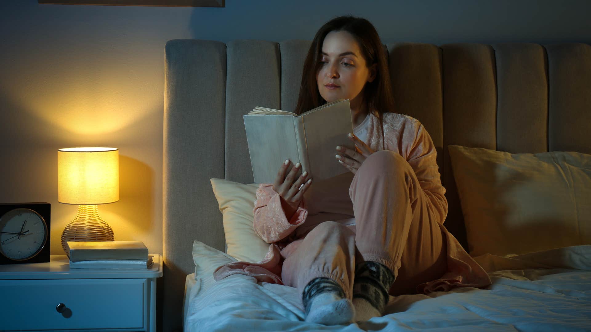 Woman without harsh lighting relaxing in her bedroom reading.