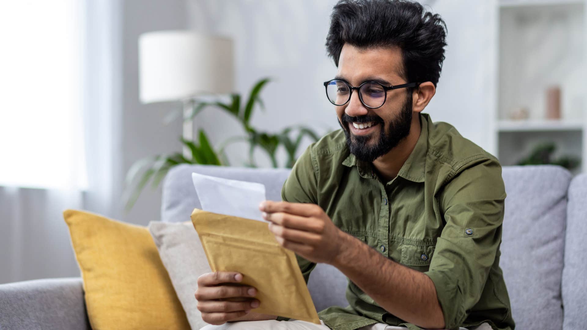 Man opening mounds of unopened mail on his couch.