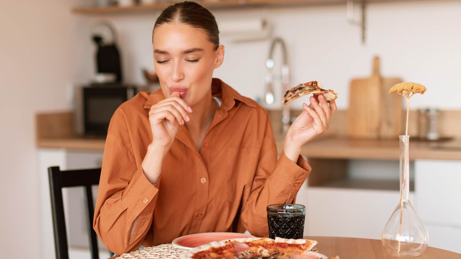 Woman licking her fingers while eating at a table