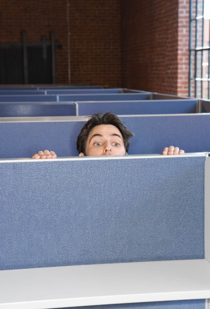 Man peeking over cubicle to see if boss has left work yet