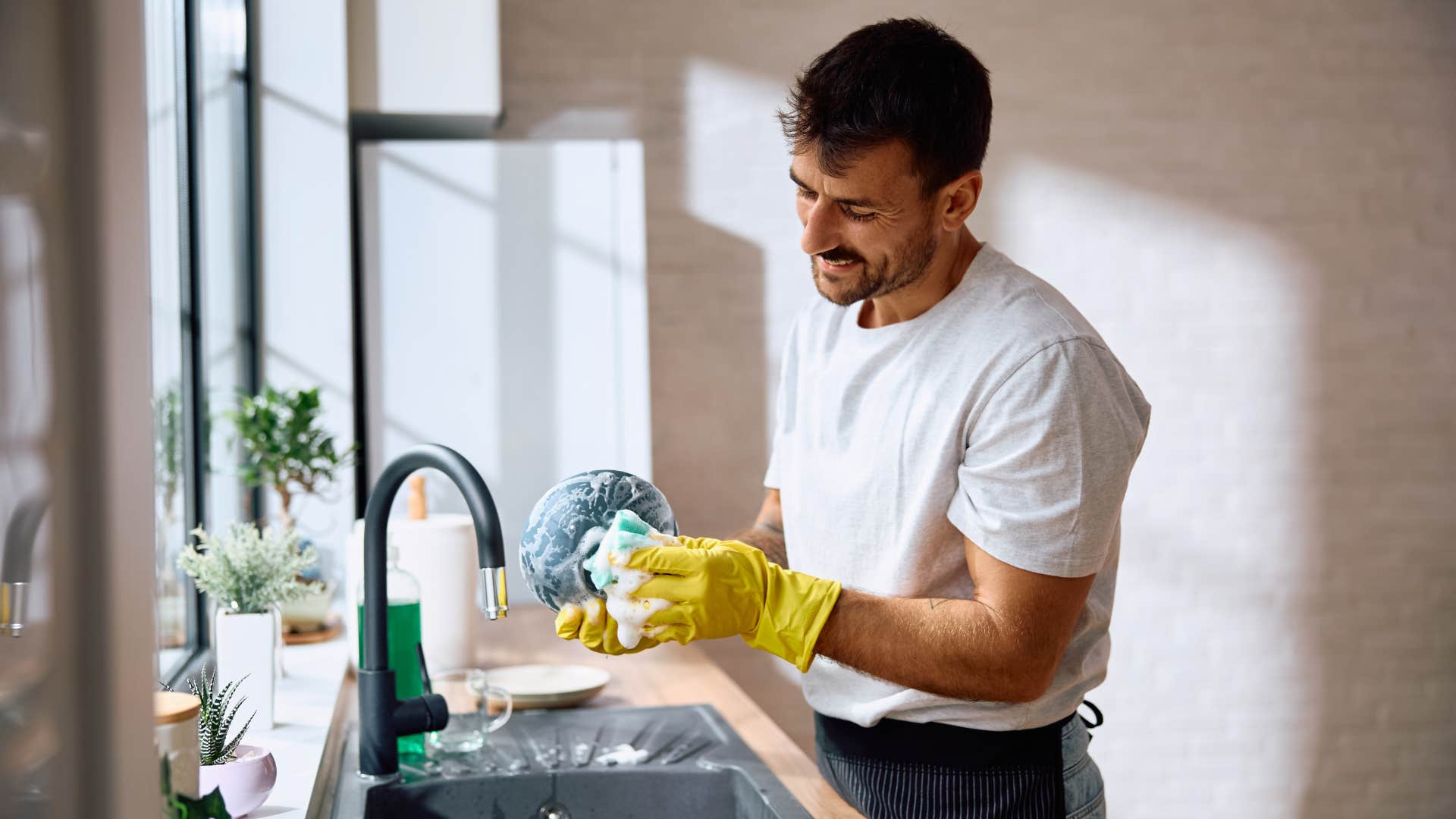 man in white shirt helping out around the house as man washes dishes in yellow gloves