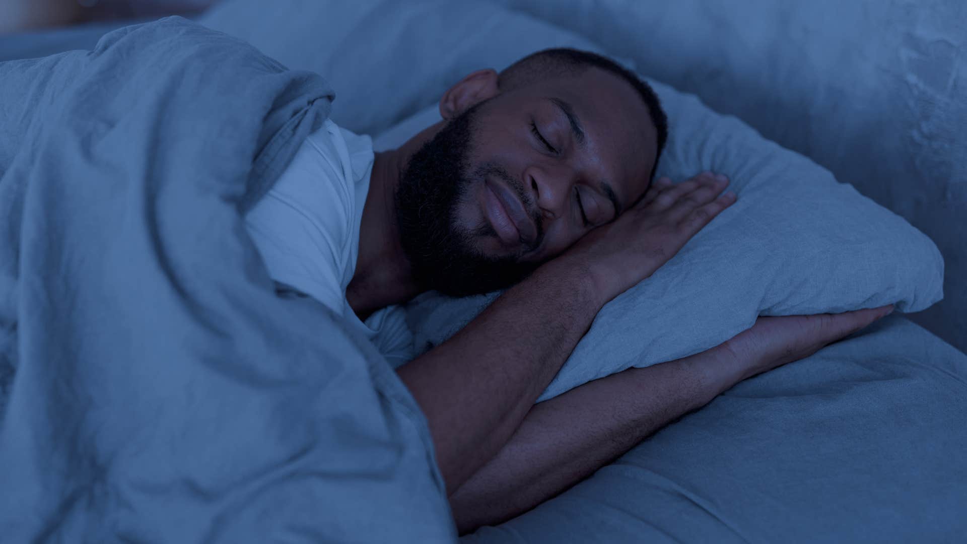 man sleeping on dirty sheets in his bed at night