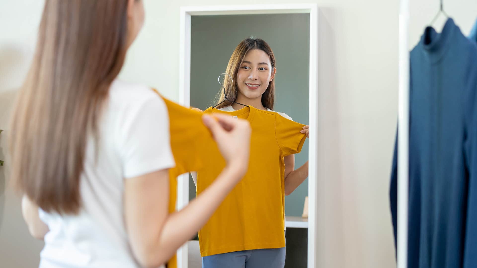 woman holding up shirt to mirror to rewear it confidently
