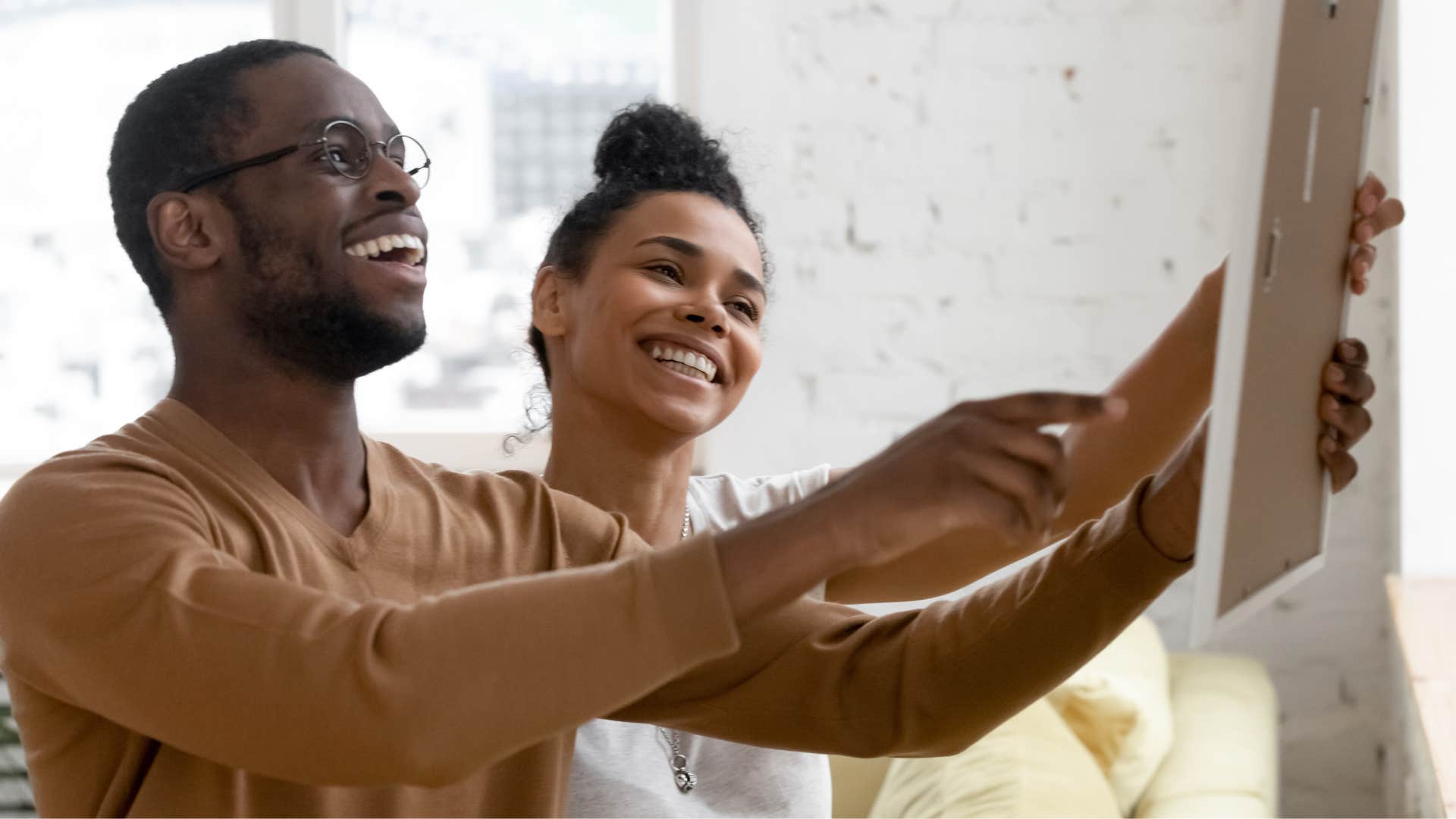 couple hanging up personal artwork and photos at home